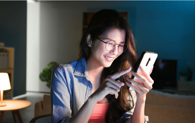 Young women wearing blue light glasses while using her phone in living room