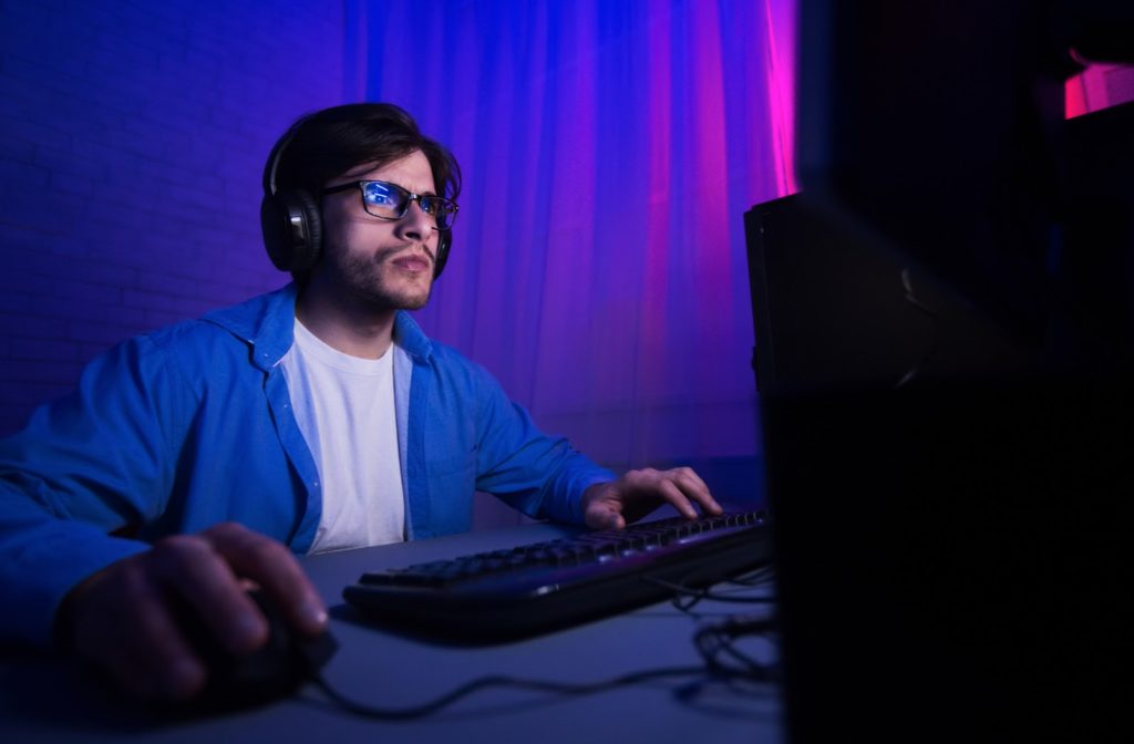 Young man wearing blue light glasses while gaming on computer