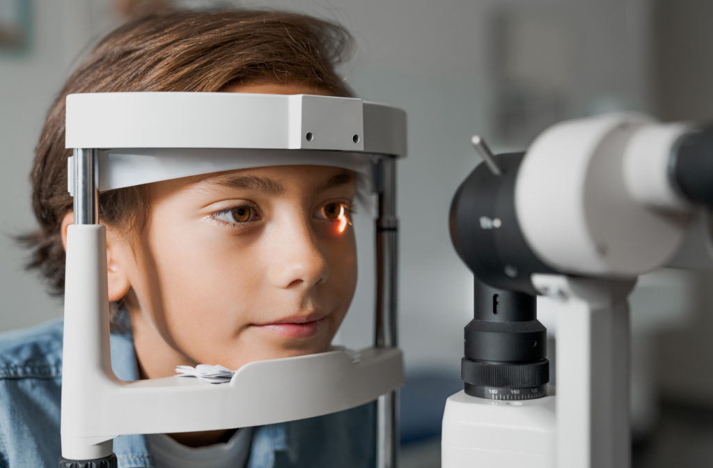 Young boy getting eye exam done at eye doctors place with light shinning through eye