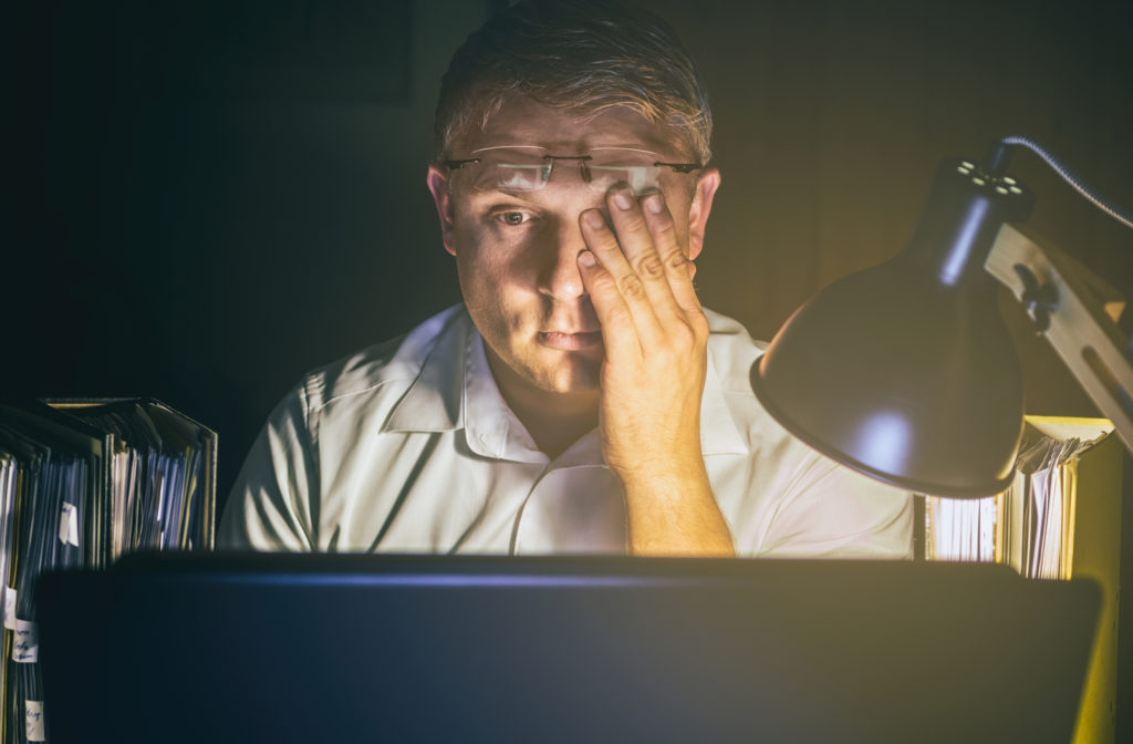 Man experiencing dry eye at night while working on laptop in office area