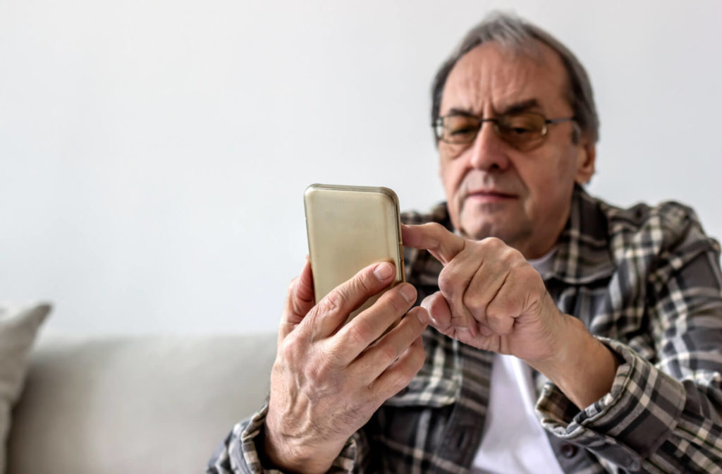 a senior man sitting on a couch squints at his phone due to vision loss from macular degeneration