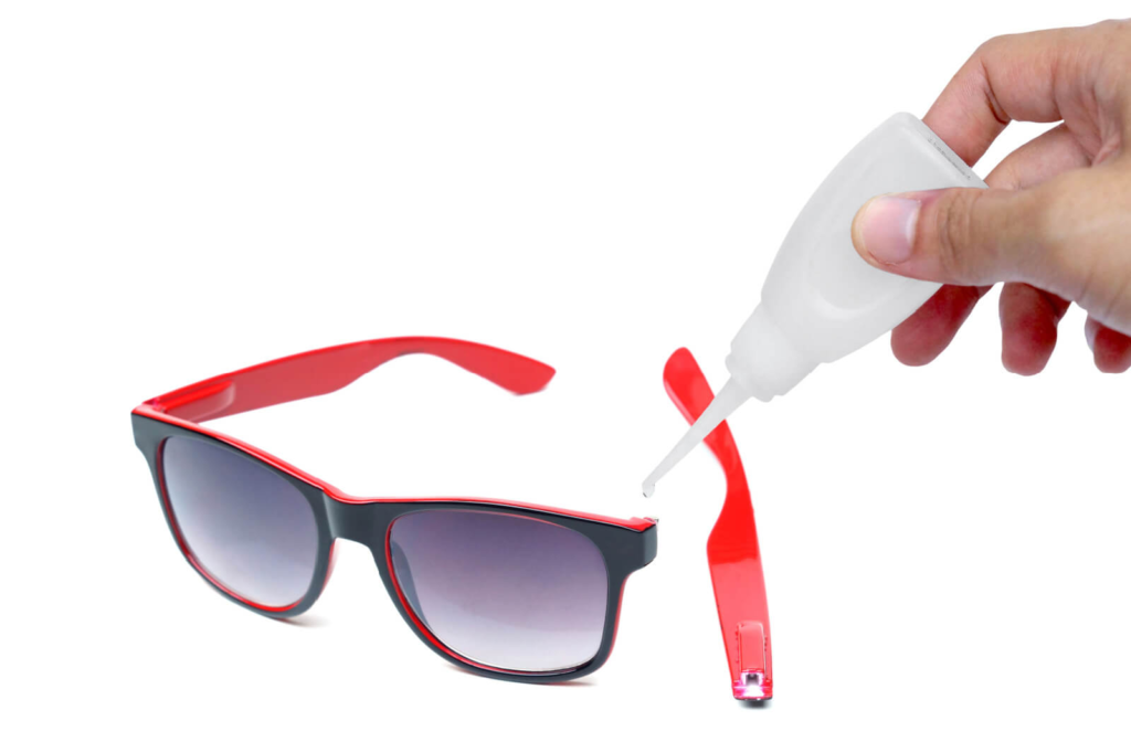 a hand applying super glue to the side of a pair of red glasses to reattach the arm