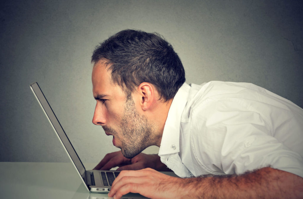 A man leans very closely to his laptop screen to better see its contents.